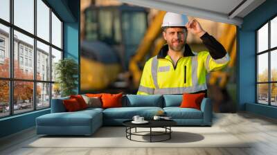 Builder near excavator. Builder worker with excavator. Builder in helmet. Worker in hardhat. Portrait mechanical worker in construction helmet. Engineer builder foreman or repairman. Wall mural