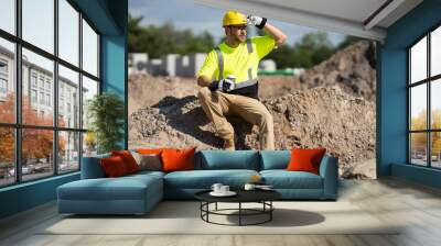 Builder rest. Construction worker with hardhat helmet on construction site. Construction engineer worker in builder uniform near construction building. Portrait of builder man in a site build house. Wall mural