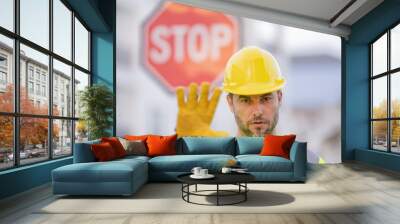 Builder showing STOP. Serious builder with stop road sign. Builder with stop gesture, no hand, dangerous on building concept. Man in helmet showing stop road sign. Wall mural