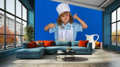 Child chef isolated on blue. Funny little kid chef cook wearing uniform cook cap and apron cooked food in the kitchen. Wall mural