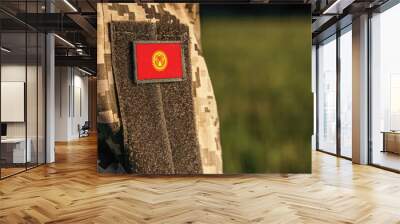 Close up millitary woman or man shoulder arm sleeve with Kyrgyzstan flag patch. Troops army, soldier camouflage uniform. Armed Forces, empty copy space for text
 Wall mural