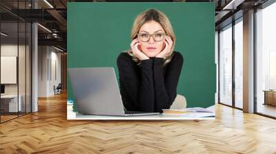 Concentrated attractive teacher. Portrait of smart young woman in glasses with book on the blackboard in class at high school or collage. Female student study in university. Wall mural