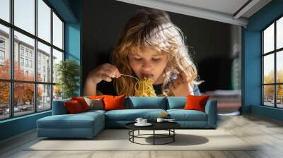 Cute child eats food itself with spoon. Cute little kid eating spaghetti pasta at home. Wall mural