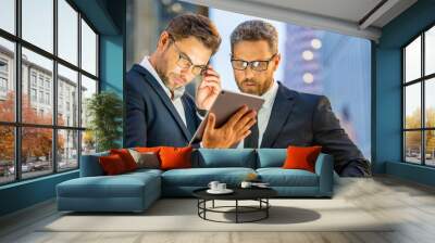 Discussing and planning remote working. Business men working on social media strategy with a digital tablet at night city. Two businessman outdoors sharing tablet, remote working, discussing. Wall mural