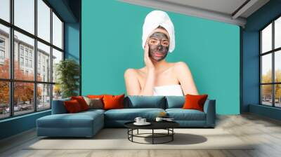 Facial mask. Skin care. Woman applying black clay mask isolated on blue studio background. Young spa model uses face care cream. Facial cream, moisturizing lifting nourishing creme. Wall mural