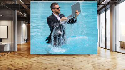 Funny business man in business suit with laptop jumping in splash water in the pool. Remote work. Crazy freelancer. Business and summer. Summer leisure weekend and remote work. Crazy business. Wall mural