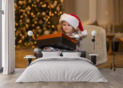 Happy child in santa hat near christmas tree at home. Wall mural