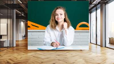 Happy teenager studying in classroom. Young attractive student with books in white uniform school shirt. School girl ready to homework. Wall mural