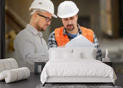 Male architect and developer discussing blueprints at construction site Wall mural