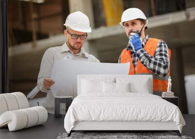 Male architect and developer with walkie talkie and blueprints at construction site Wall mural