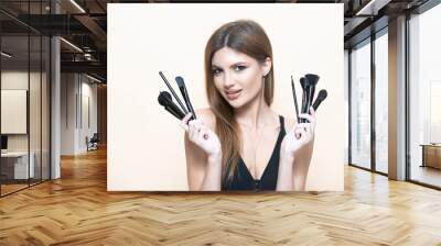 Make up artist with with makeup brushes. Portrait of attractive young woman holding various make-up brushes. Professional makeup artist. Makeup artist applies powder and blush. Beautiful woman face. Wall mural