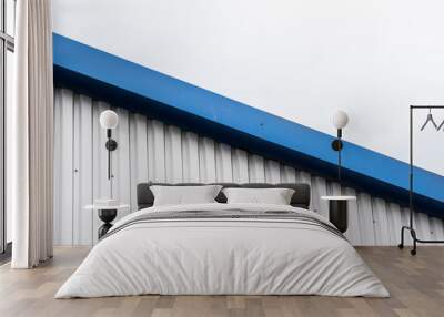 Metal corrugated sheets on a building with a blue metal corners. White aluminium metal corrugated roof or wall sheets against cloudy sky background on a factories and industrial buildings. Wall mural