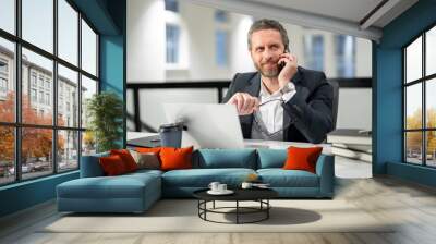 Office worker with laptop at office. Ofice employee remote working in modern office. Businessman on remote meeting, working online in offices place. Business man talking on phone at office workplace. Wall mural