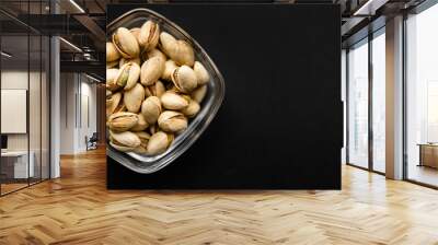 Pistachios in a small plate on a black table. Pistachio is a healthy vegetarian protein nutritious food. Natural nuts snacks. Wall mural