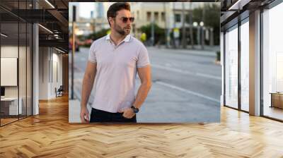 Portrait of handsome male model outdoor. Stylish man dressed in polo. Fashion male posing on the street background. Urban style. Young man walk through the city. Wealthy businessman posing next to Wall mural