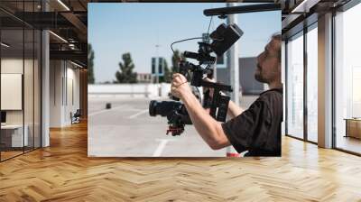 Professional videographer holding camera on 3-axis gimbal which mounted on easy rig. Videographer using steadicam. Pro equipment helps to make high quality video without shaking. Wall mural