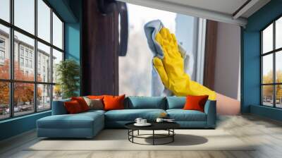 A female hand in bright yellow rubber gloves washes. cleaning the window with a soft rag. Wall mural