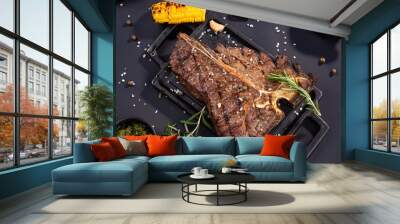 Delicious beef steak on black stone cutting board. Grilled meat served with grilled corn, garlic, rosemary, sauces and salt Wall mural