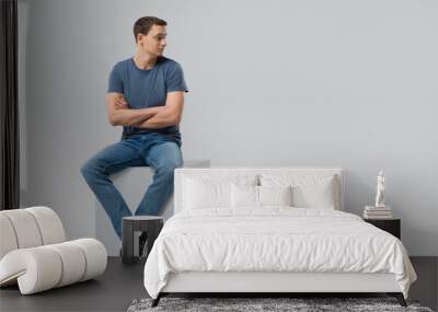 Man sitting on a cube and looking away - isolated Wall mural