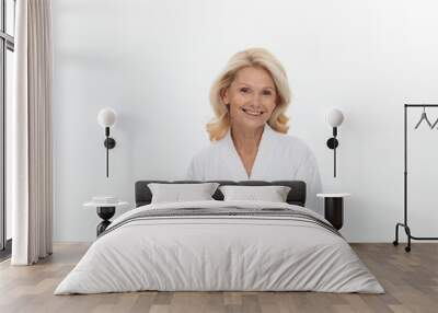 Portrait of beautiful adult woman with blond hair wearing white bathrobe smiling at camera over white background Wall mural