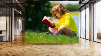 Smart child boy reading book in park outdoor. Blonde kid reading a book in summer. Clever kids outdoor portrait. Kids imagination, innovation and inspiration. Outdoor school, learning kids. Wall mural