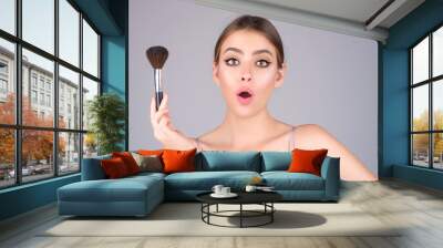 Studio portrait of a woman applying cosmetic tonal foundation on face using makeup brush. Beautiful girl doing contouring apply blush on cheeks isolated on studio background. Wall mural