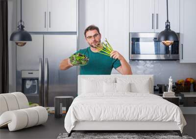 Taking care of health. Handsome man in the kitchen at home. Young man cooking vegetables in the kitchen. Dieting man with bowl of salad. Green salad healthy food concept. Healthy dinner. Wall mural