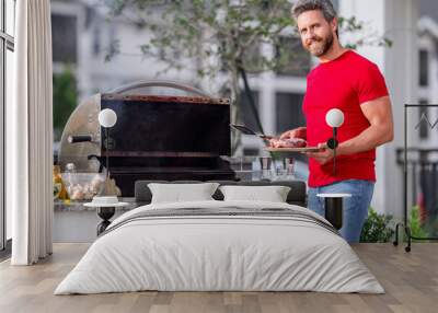 The barbecue. Man preparing barbecue grill outdoor. Man cooking tasty food on barbecue grill at backyard. Chef preparing food on barbecue. Millennial man grilling meat on grill. Bbq. Meal grilling. Wall mural