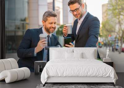 Thoughtful businessman wearing a suit front of office outdoor. Business man standing in front of city skyscraper. Two business men using phone outdoor. Wall mural