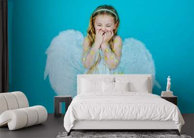 Valentines Day. Looks like an angel. Angel kid with blonde curly hair. Cute child girl in white dress standing over color background. Portrait of beautiful angel little girl with angels wings. Wall mural