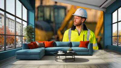 Worker in helmet on site construction. Man excavator bulldozer worker. Construction driver worker with excavator on the background. Construction worker with tractor or construction at building. Wall mural