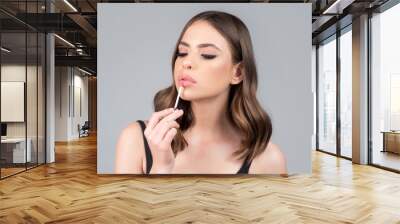 Young beautiful model with beauty face applying makeup. Fashion girl make up. Young woman applies lipstick on lips. Cosmetology, beauty and fashion. Wall mural