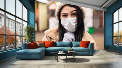 Young pretty woman celebrating dressed warm coat mittens wear blue face medical disposable mask. Cold weather, winter market holidays fair, travel resort. New Year Christmas decorations
 Wall mural