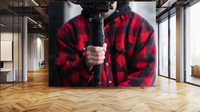 Young Professional videographer holding professional camera on 3-axis gimbal stabilizer. Pro equipment helps to make high quality video without shaking. Cameraman wearing red shirt making a videos. Wall mural