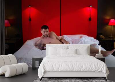 Young sexy man lying on a bed. Handsome young man with naked body, bare torso, undressed. Muscular young man laying on bed with naked muscular body. Sexy young male model. Wall mural