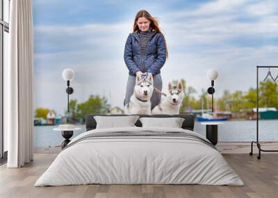 Young beautiful girl with red hair is sitting on a pier with two husky dogs. Woman with a pair of Siberian Husky Wall mural