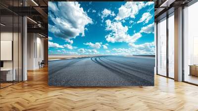 Blue sky with fluffy white clouds over a car racing track on a sunny day Wall mural