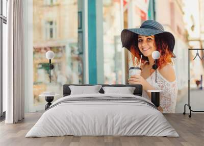 Pretty girl with red hair in a black hat is drinking take away c Wall mural