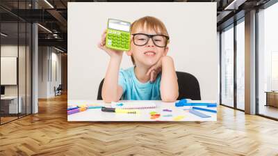 Smart boy using calculator. Kid in glasses figuring out math problem. Developing logical skills. Happy school boy doing homework. Smart kid in glasses at table with school supplies. Back to school. Wall mural