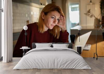 Concerned woman reviewing documents while working from her home kitchen Wall mural