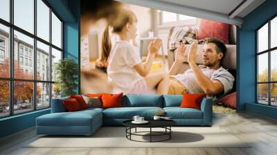 Father playing with daughter at home and clapping hands Wall mural