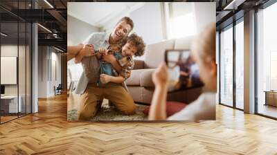 Father playing with son while being photographed by daughter at home Wall mural