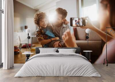 Happy family moment with mother taking photo of father playing with son in living room Wall mural