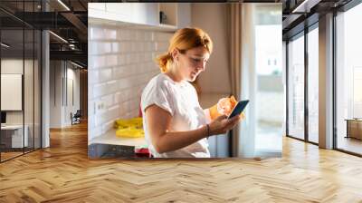 Housewife taking break from cleaning check smartphone in modern kitchen Wall mural