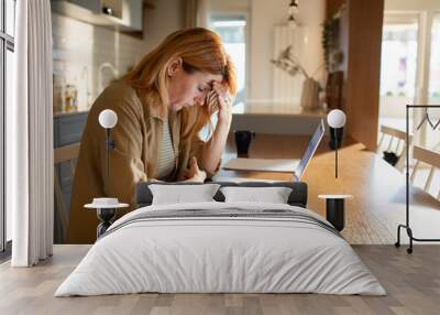 Stressed young woman using laptop to pay bills at home Wall mural