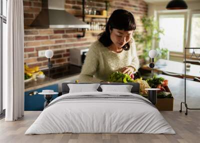 Woman taking vegetables out of cardboard box in kitchen at home Wall mural