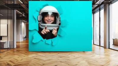 Small child in wearing an airplane helmet looking through a hole of colored paper Wall mural