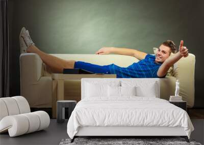 Young man relaxing on couch making thumb up Wall mural