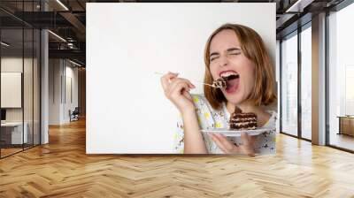 Funny young girl eating tasty chocolate cake over white background. Empty space Wall mural