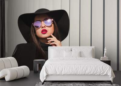 Glamorous brunette model in mirror glasses and broad brimmed hat posing near the shutters Wall mural